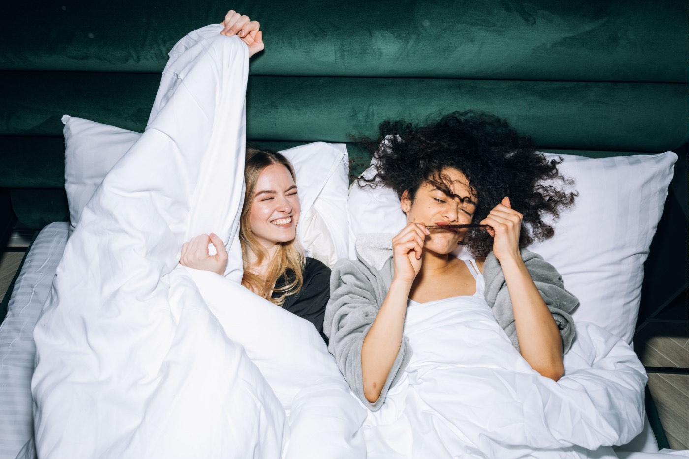 Two friends laughing in a hotel bed